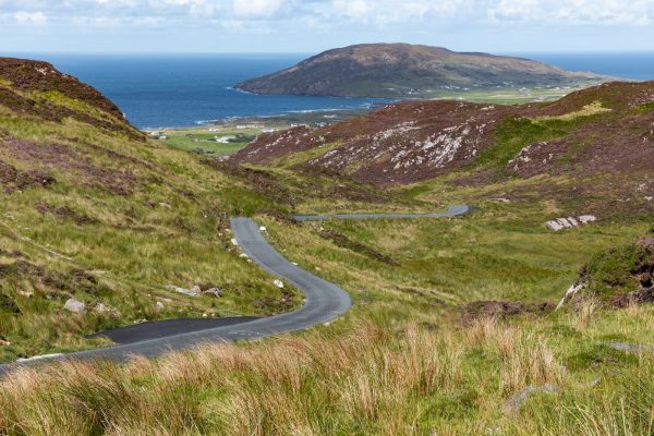 gray asphalt road on green mountain beside body of water during daytime